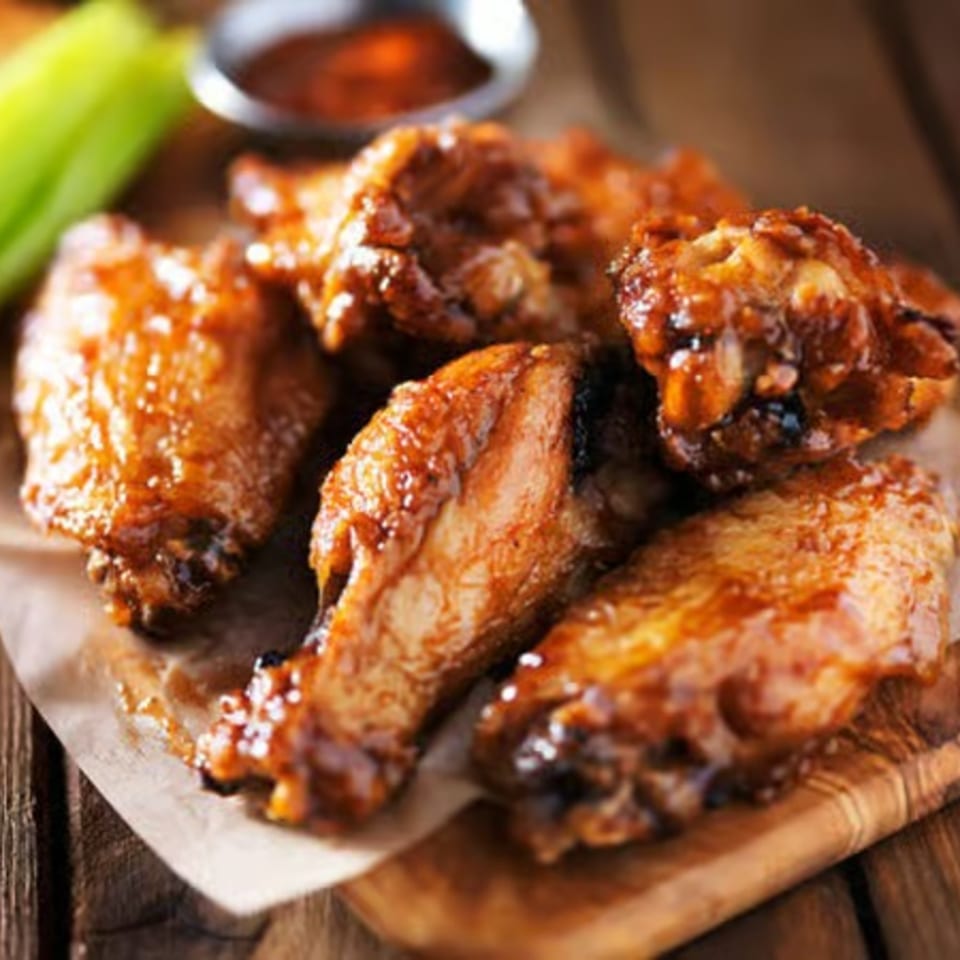 Glazed chicken wings on parchment paper with a side of celery and dipping sauce.