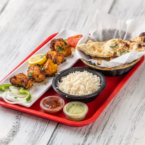 Indian chicken tikka, rice, naan bread, and sauces on a red tray.