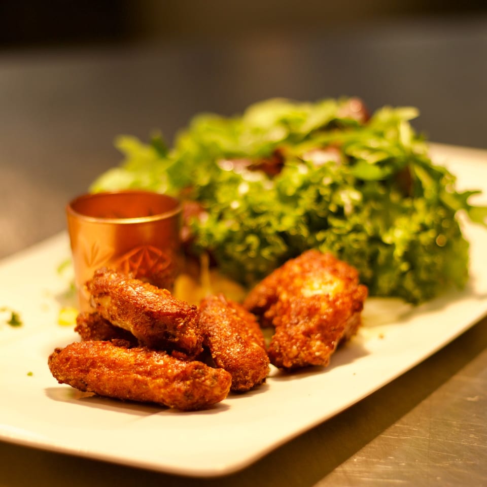 Crispy fried chicken wings with a side salad and a copper dipping sauce cup on a white plate.